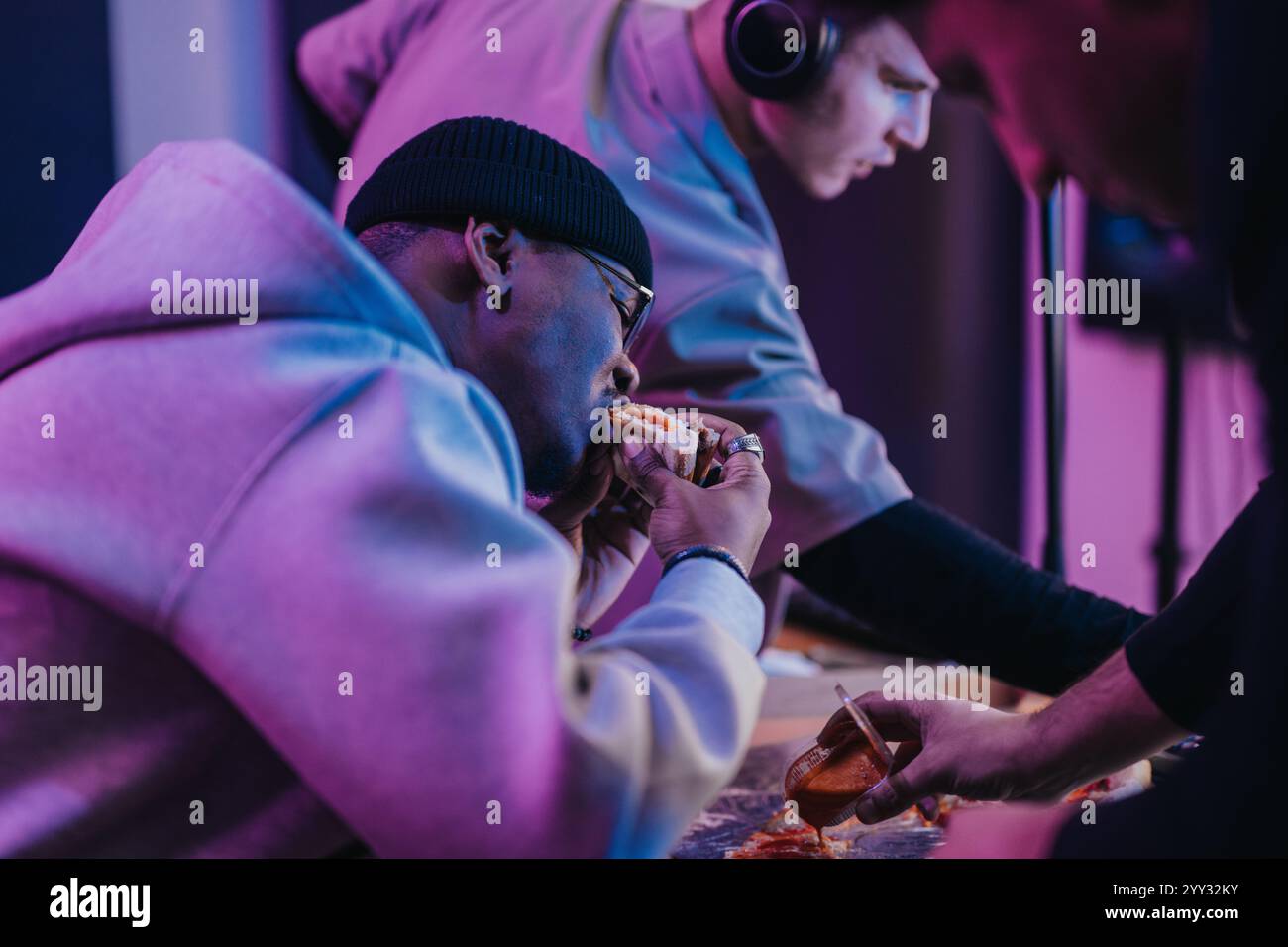Eine Gruppe von Freunden, die während der Arbeit in einem Musikstudio einen verspielten Moment beim Essen verbringen. Stockfoto