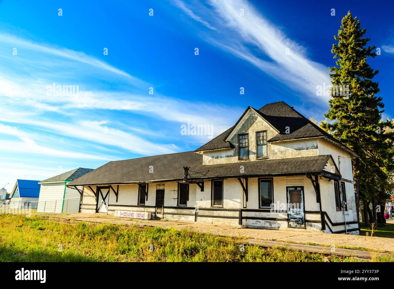 Ein großes weißes Haus mit einem schwarzen Dach liegt auf einem grasbewachsenen Feld. Das Haus ist von Bäumen umgeben und er wird verlassen. Der Himmel ist klar und blau, und der Stockfoto