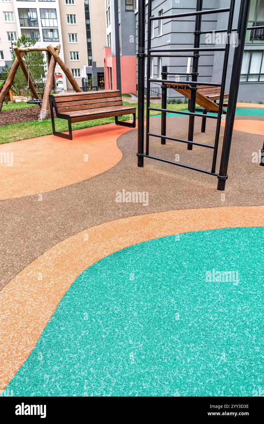 Spielplatz mit lebhaftem Gummifußboden, Bänken und Kletterausrüstung, umgeben von Gebäuden, für Aktivitäten im Freien Stockfoto