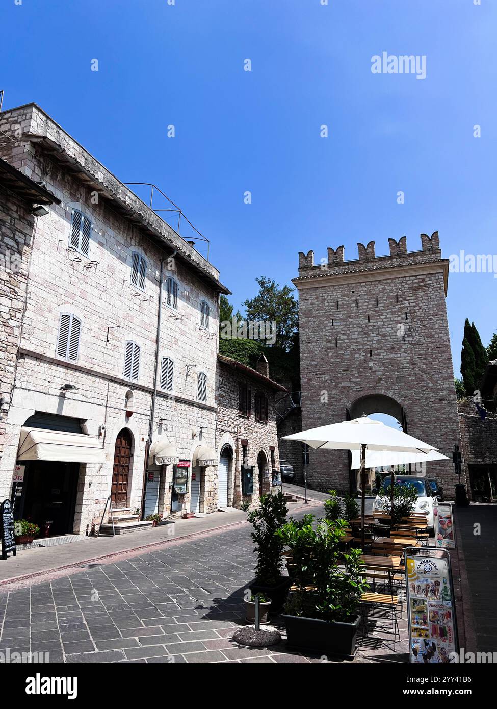 Diese malerische italienische Straße verfügt über historische Steinhäuser, ein malerisches Café im Freien mit Sonnenschirmen und einen hellblauen Himmel. Perfekt zum Vorführen Stockfoto