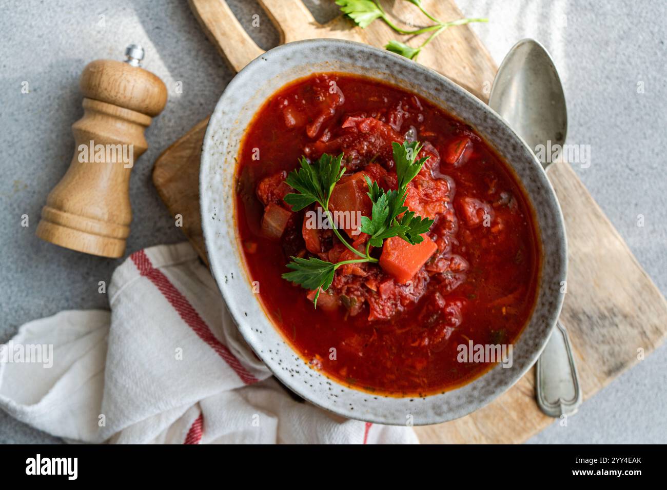 Blick von oben auf die traditionelle ukrainische Rote-Beete-Suppe Borscht, serviert in einer rustikalen Keramikschale umgeben von frischen Kräutern und einer alten Pfeffermühle, gefangen genommen Stockfoto