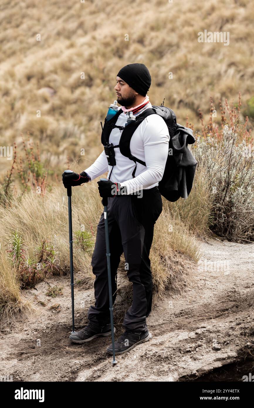 Der schwarze Mann trägt Bergsteiger-Ausrüstung auf einem Wanderweg in Wanderkleidung und steht mit Trekkingstöcken und fängt den Geist des Abenteuers in einer Natur ein Stockfoto