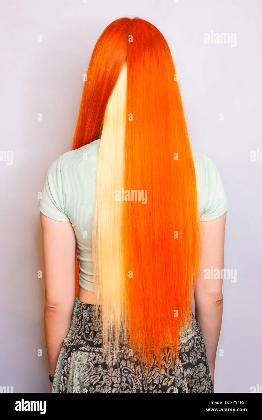 Rückansicht von leuchtend langen orangefarbenen Haaren mit auffälligem blondem Streifen, ideal zur Präsentation kreativer Haarfarben, Mode und Styling-Techniken Stockfoto
