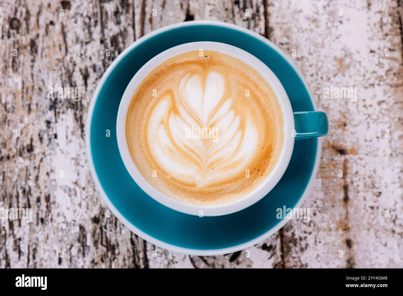 Blick von oben auf einen Cappuccino in einer blauen Tasse mit komplizierter Latte Art auf einem rustikalen Holztisch. Die ruhige Komposition unterstreicht den Kaffeekultu Stockfoto
