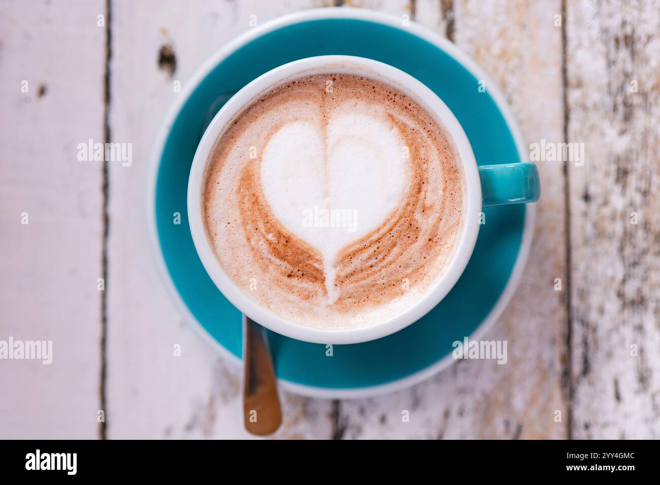 Eine Nahaufnahme eines herzförmigen Latte Art Designs in einem schaumigen Kaffee, serviert in einer türkisfarbenen Tasse vor einem verstörten Holztisch. Perfekt für Konzepte von Stockfoto