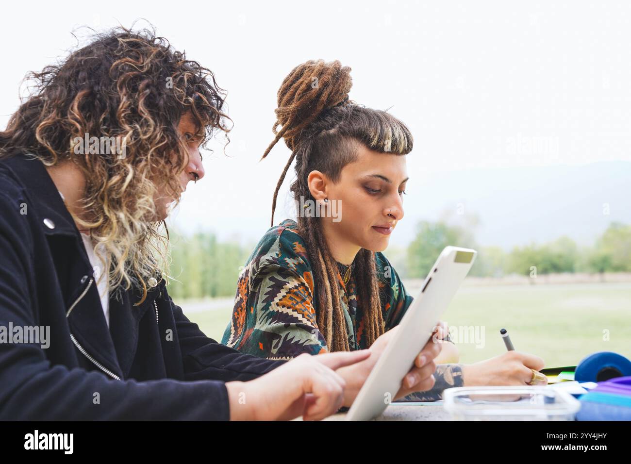 Eine Transgender-Agentin mit Dreadlocks und einem Pony, zusammen mit einer lockigen Transgender-Frau, die draußen zusammen arbeitet. Beide sind eng Stockfoto