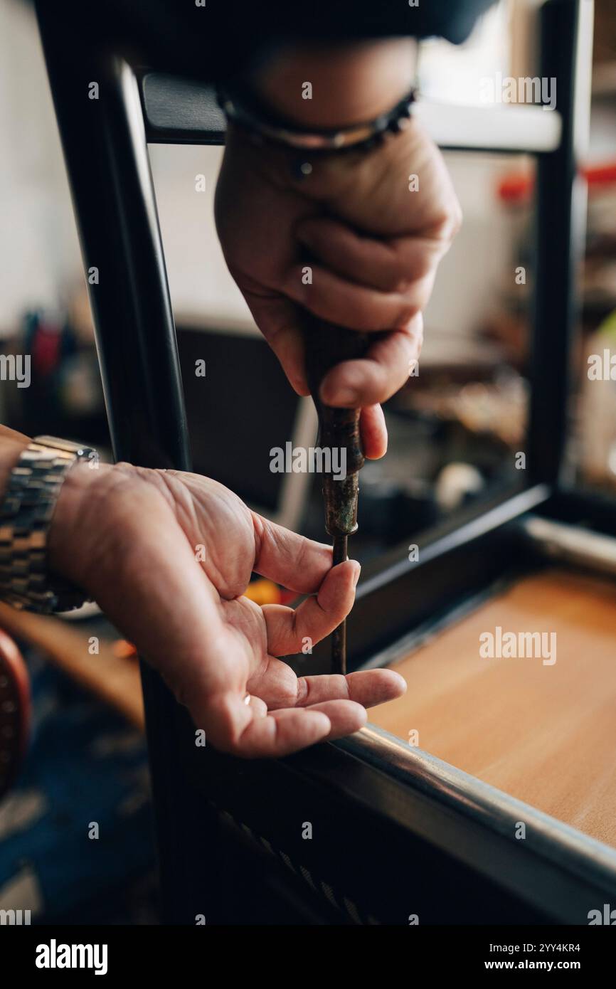 Hände eines älteren männlichen Besitzers, der Stuhl mit Werkzeug repariert, während er im Antiquitätengeschäft arbeitet Stockfoto