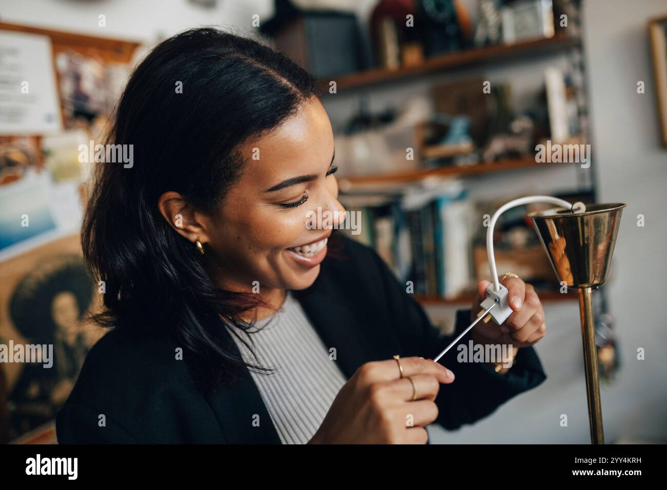 Lächelnde weibliche Besitzerin repariert den Stecker der Lampe, während sie im Antiquitätengeschäft arbeitet Stockfoto