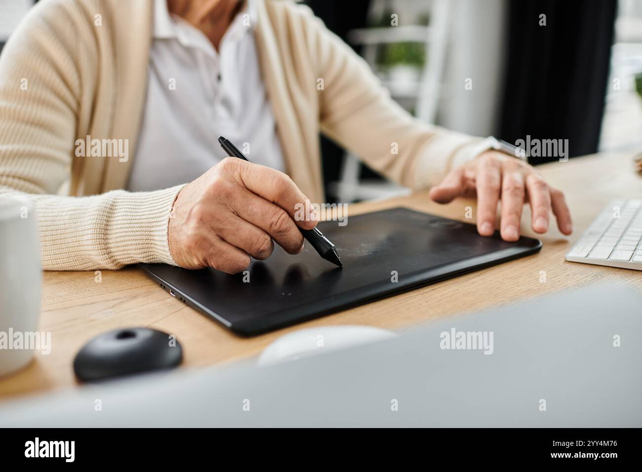 Der gutaussehende Senior man kreiert digitale Kunst mit einem Tablet in einer hellen, eleganten Büroumgebung. Stockfoto
