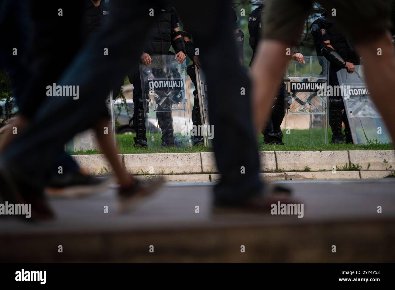 Die Aufständischen-Polizei hält Schutzschilde und Schlagstöcke. Foto durch die Beine von wandelnden Demonstranten. Stockfoto