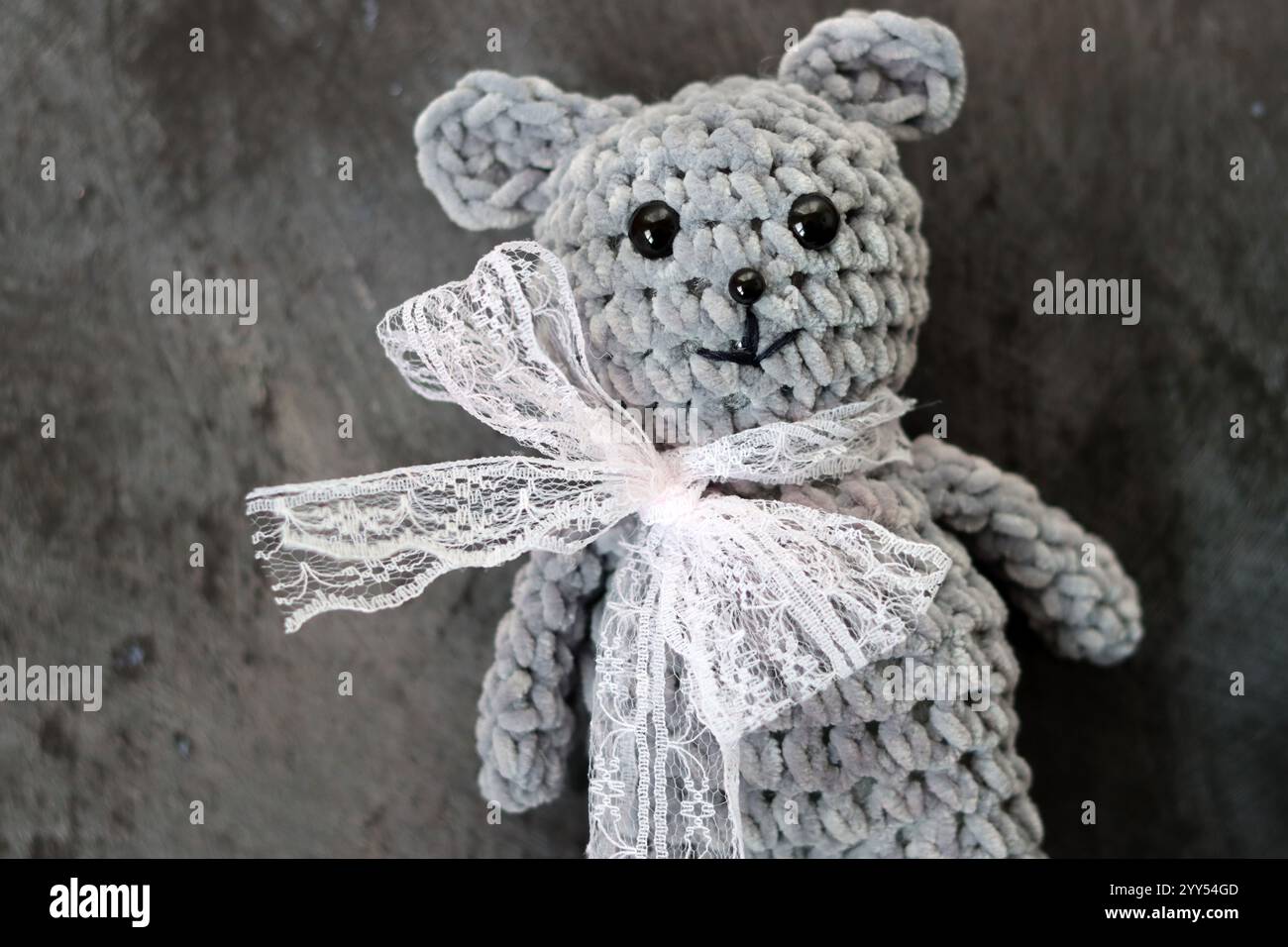 Handgemachter Häkelteddybär mit Schleife auf grauem Hintergrund Stockfoto