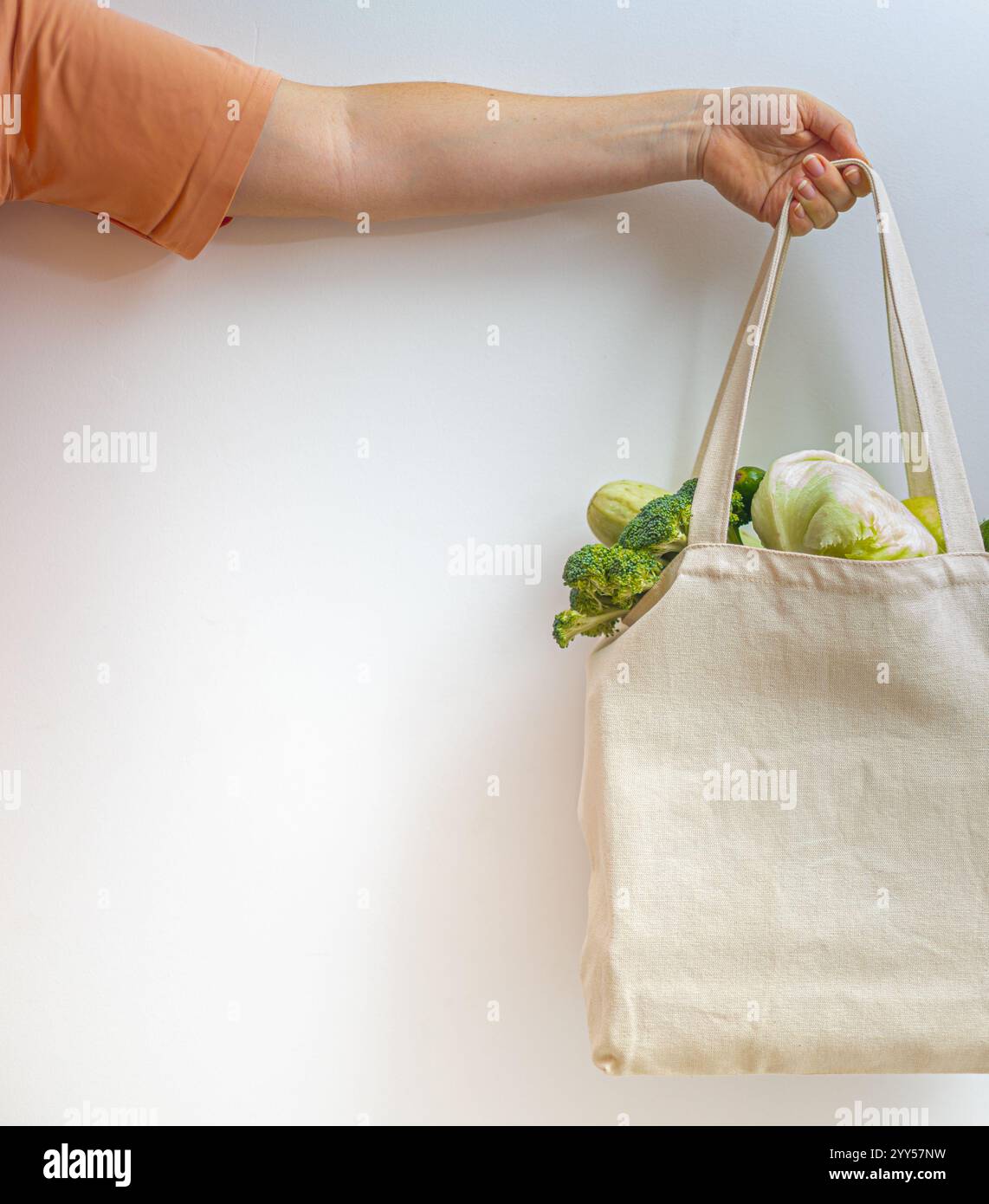 Eine Hand, die einen Baumwollbeutel mit Gemüse und Grünpflanzen vor weißem Hintergrund hält, was einen umweltfreundlichen Lebensstil und die Ablehnung von symbolisiert Stockfoto