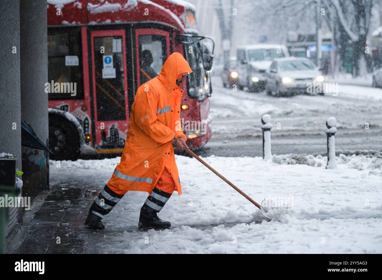 Mitarbeiter des kommunalen Dienstes reinigt Schnee mit Schaufel von Straße und Bürgersteig. Reinigung von Straßen und Straßen während Schneesturms. Stockfoto