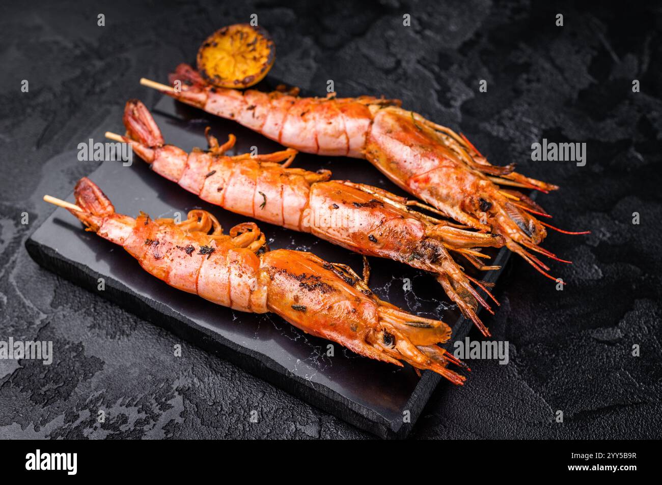 Garnelenkebab, Spieße mit gegrillten roten Garnelen Langostino Austral. Schwarzer Hintergrund. Draufsicht. Stockfoto