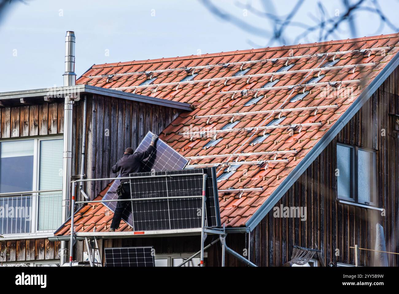 Auf einem Passivhaus aus Holz montiert ein Monteur Solarpanele auf dem Dach. Leutkirch, Baden Württemberg, Deutschland Montage von Solarpanelen Stockfoto