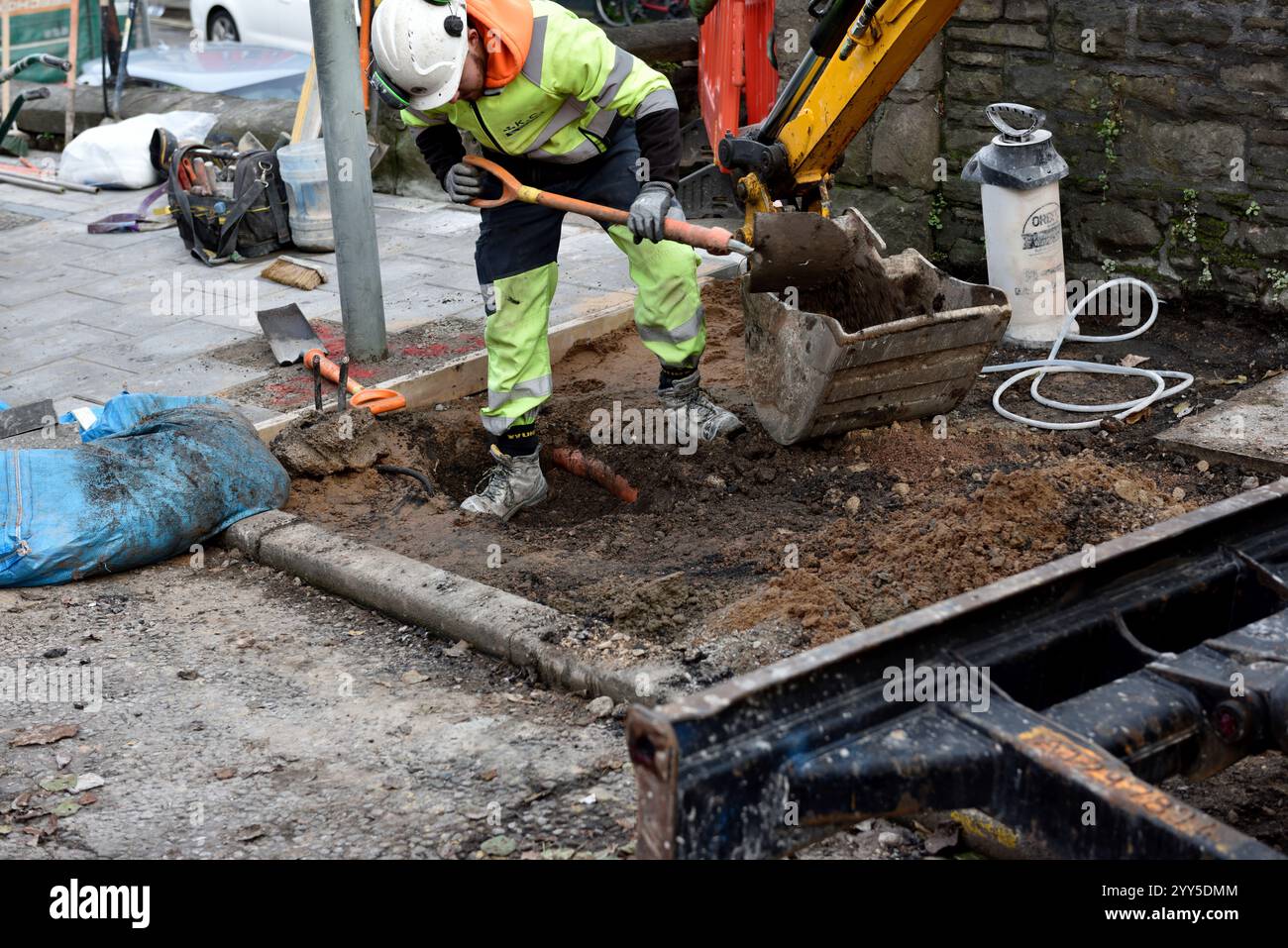 Arbeiter graben ein Loch, um die Leitung freizulegen, und Schaufeln in Baggerlöffel auf dem Asphalt während Bauarbeiten Stockfoto
