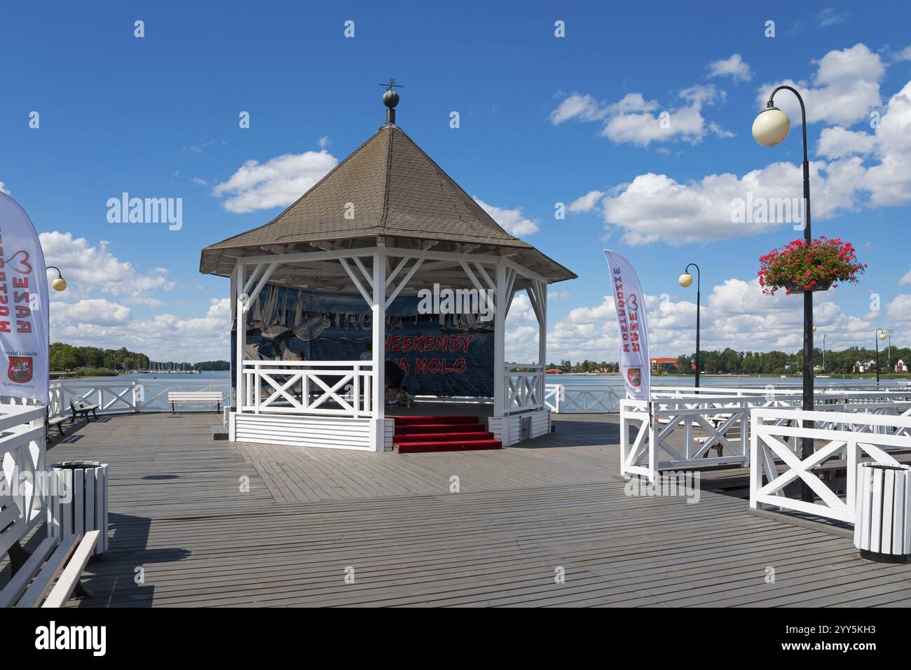 Holzpavillon auf einer Fußgängerbrücke über einem See unter blauem Himmel mit Wolken, Drawenzsee, Jezioro DrwEckie, Ostroda, Osterode in Ostpreußen, Warminsko- Stockfoto