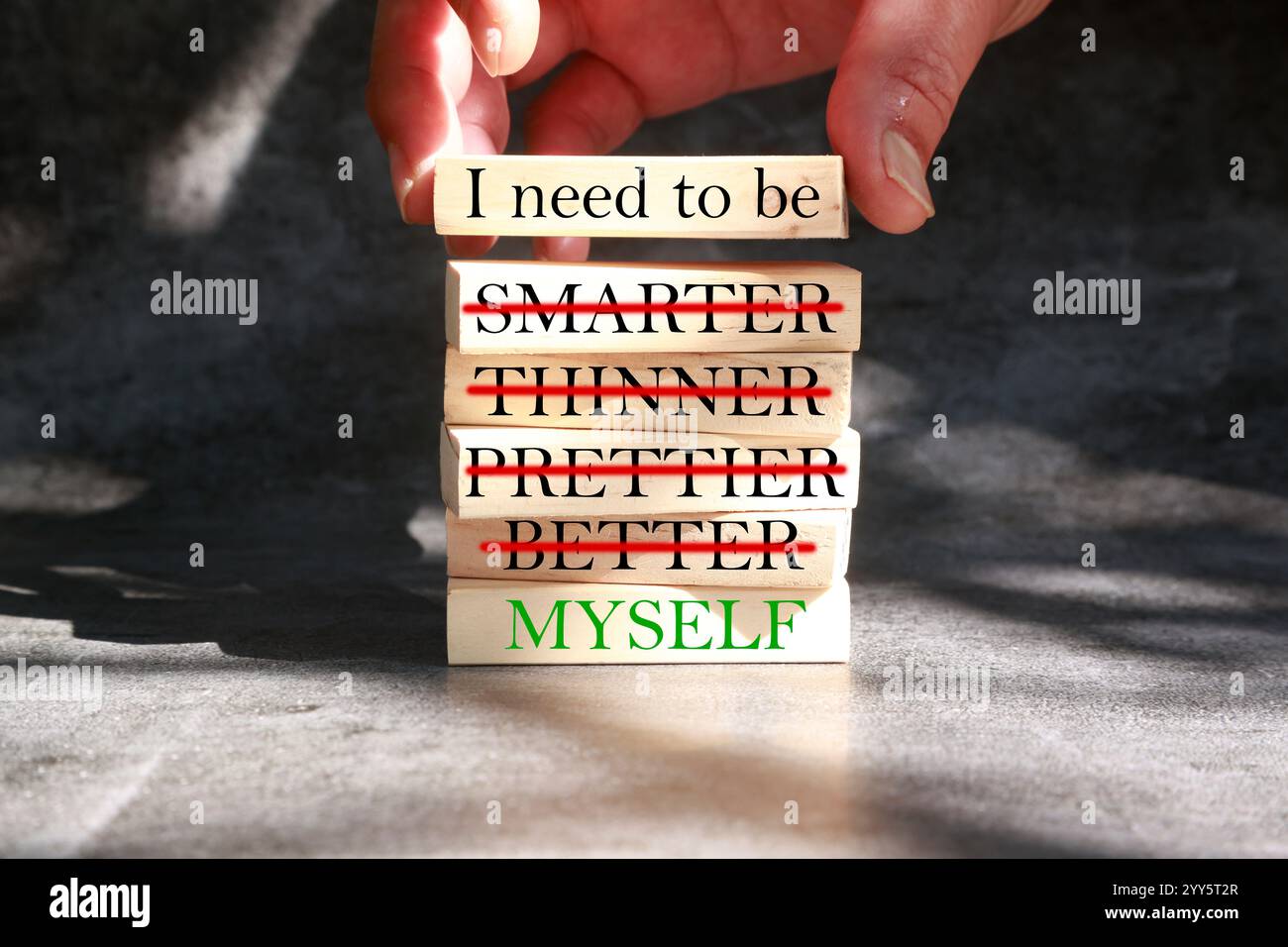 Sei ich-Symbol. Geschäftsmann Hand. Holzblöcke mit den Worten „ich muss ich selbst sein, nicht intelligenter, dünner, hübscher, besser“. Schöner grauer Hintergrund. Stockfoto