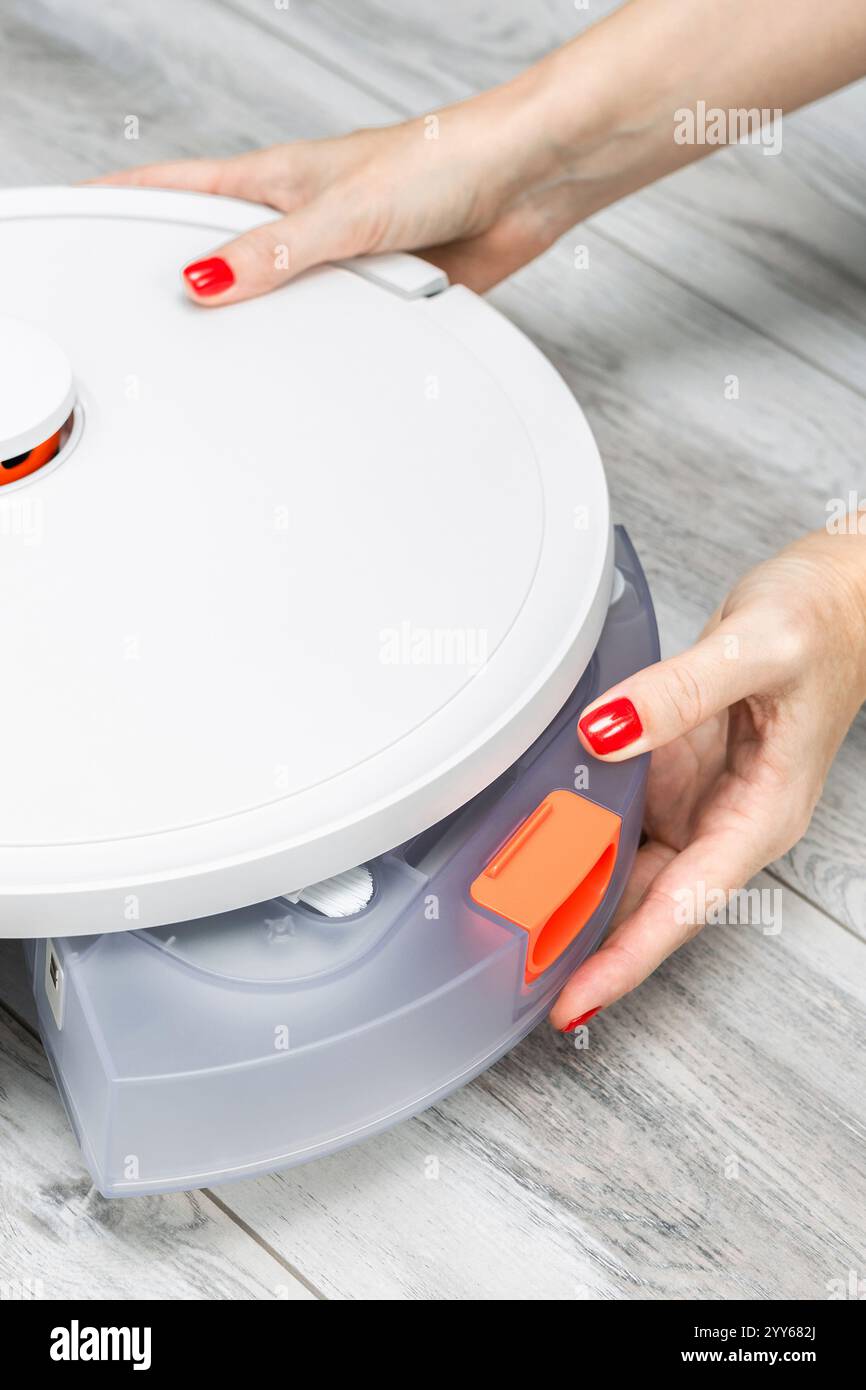 Frau, die den Staubbehälter vom Roboter-Staubsauger entfernt, vertikales Foto. Stockfoto