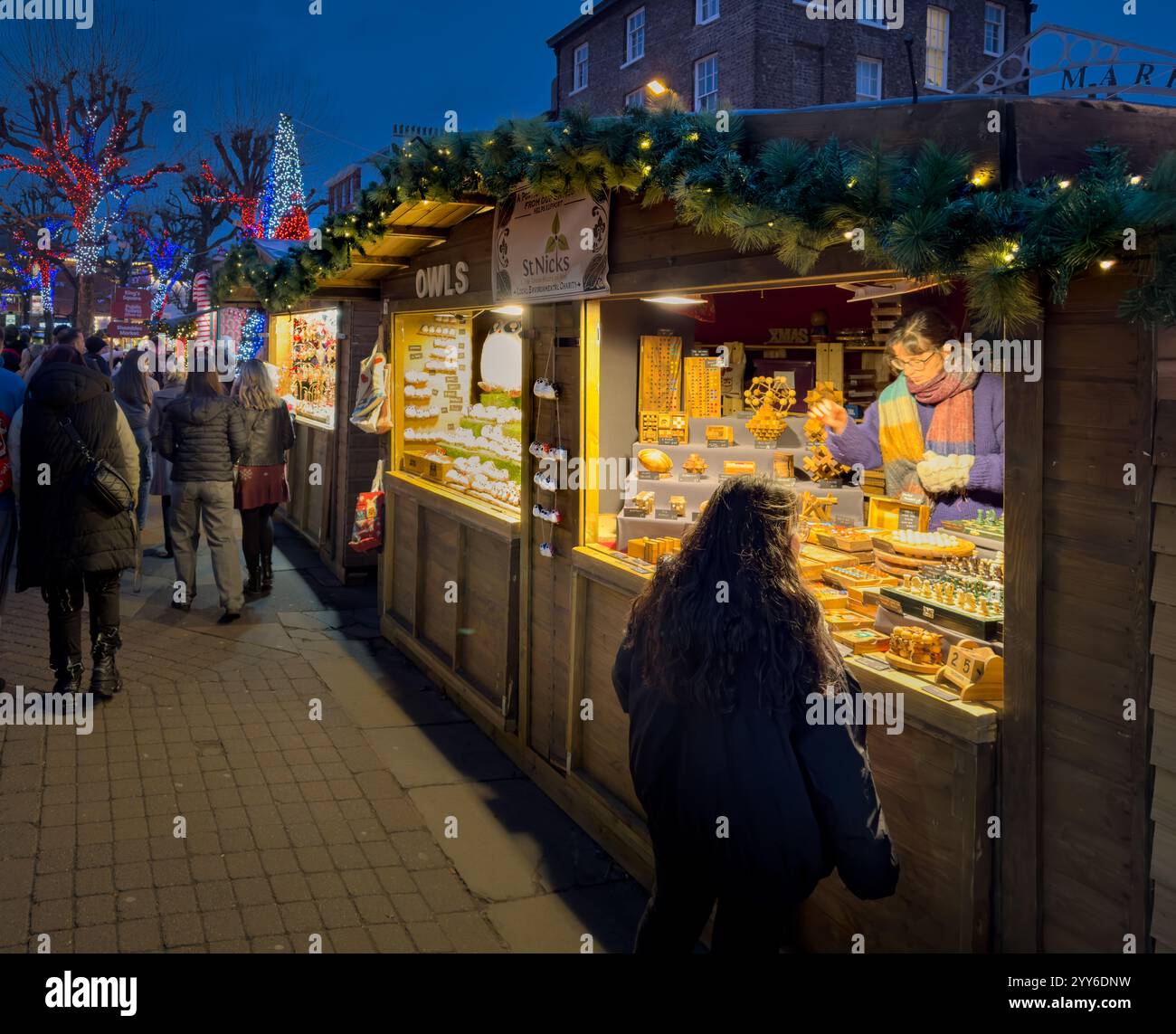 Besucher genießen Shopping und bummeln in den festlichen Ständen des Yorker Weihnachtsmarktes, während die Dämmerung mit Lichtern und Weihnachtsstimmung einbricht. Stockfoto