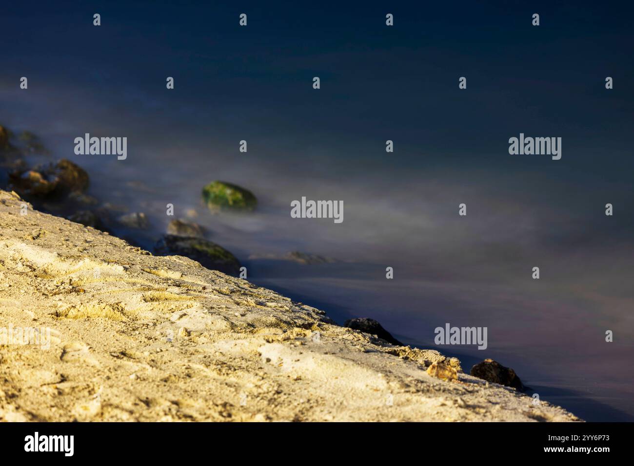 Nahaufnahme der nächtlichen Sandstrandküste mit kleinen Felsen und ruhigem karibischem Meer, Aruba. Stockfoto