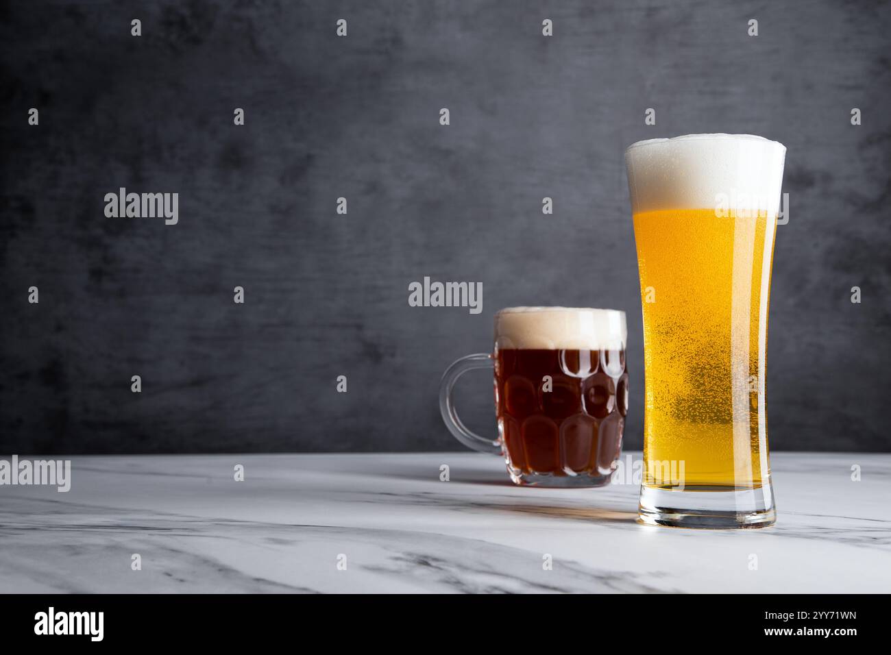 Zwei Gläser Golden Yellow Blonde und Amber Ale Biergetränke mit großen köstlichen Schaumstoffköpfen und grauer Kulisse Stockfoto
