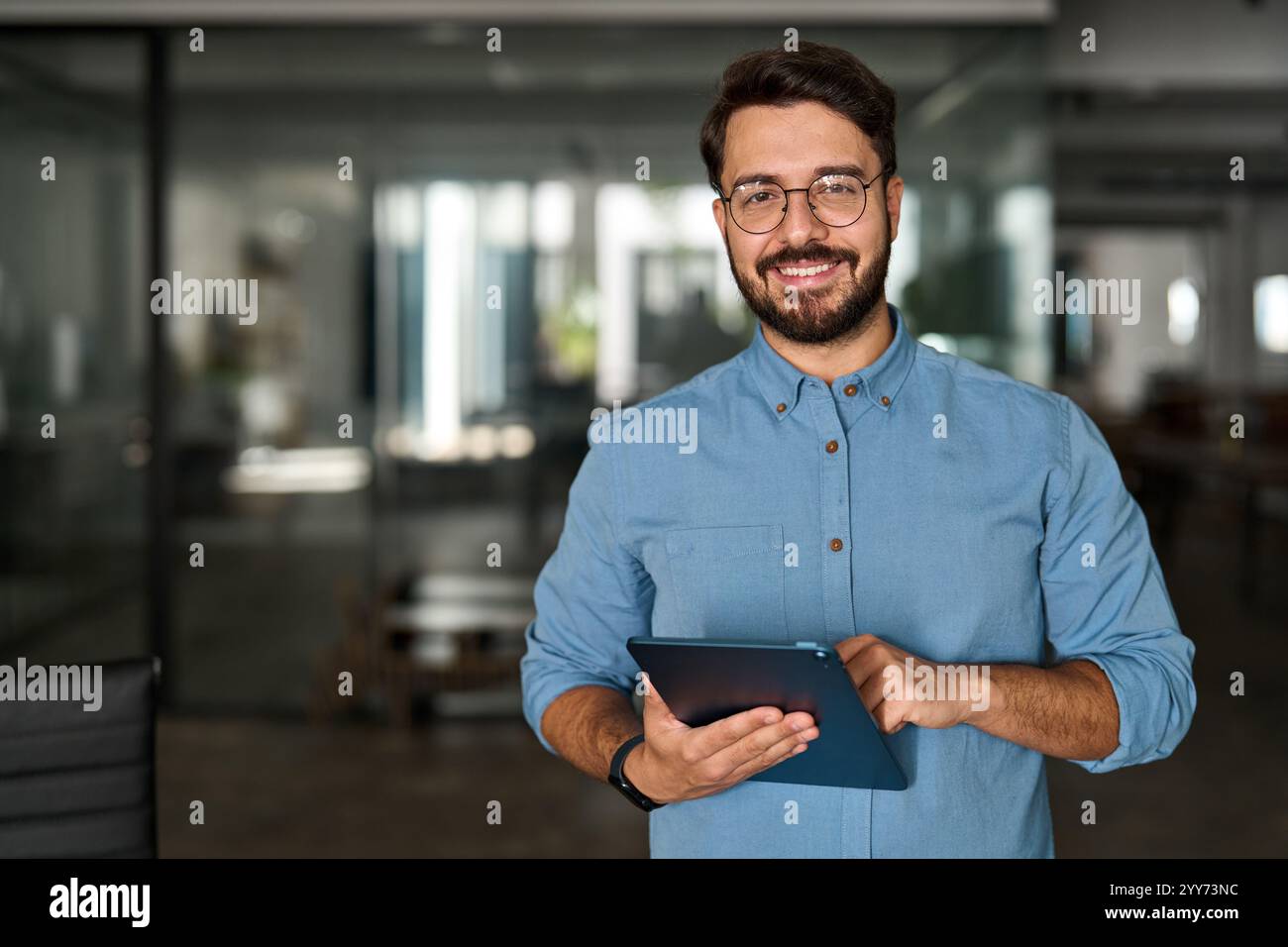 Glücklicher junger professioneller Geschäftsmann, der bei der Arbeit mit einem Tablet auf die Kamera blickt. Stockfoto