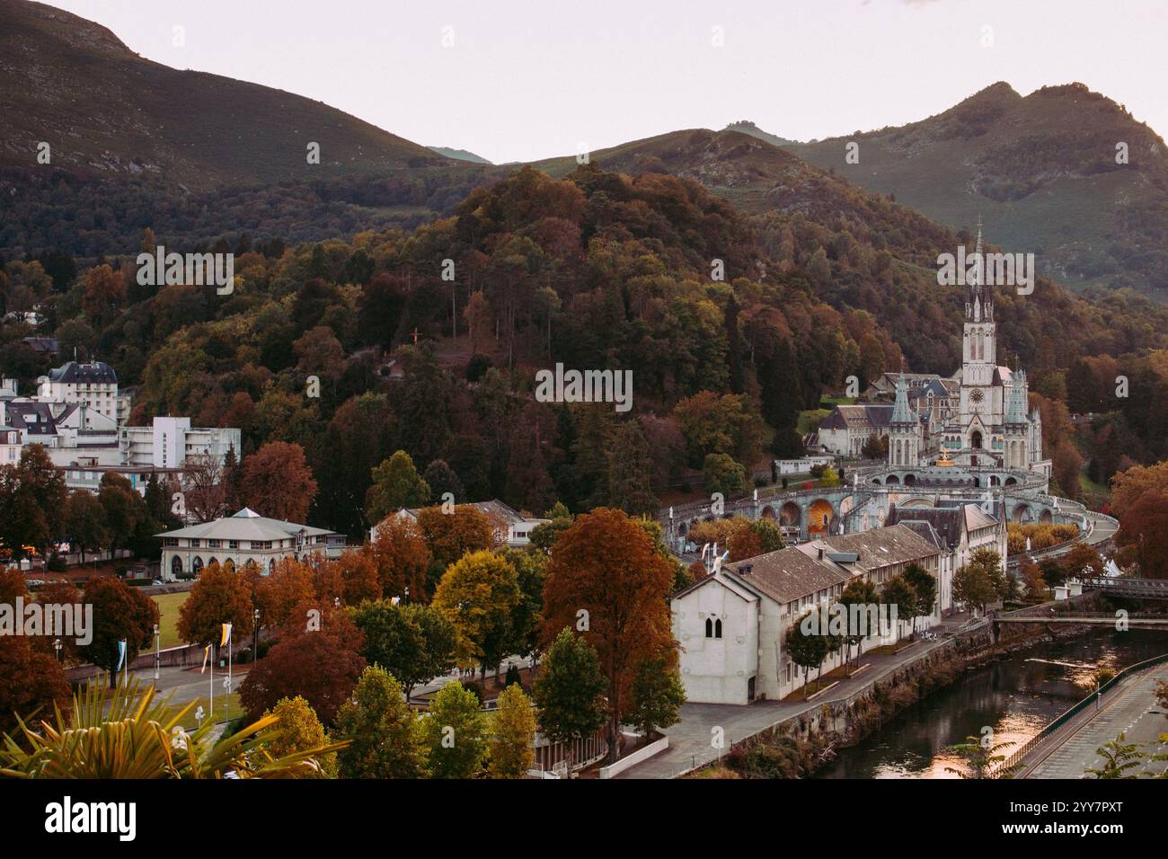 Lourdes Wahrzeichen im Abendhimmel. Kathedrale unserer Lieben Frau von Lourdes mit Fluss und Bergen. Berühmtes Pilgerzentrum. Rosenkranzheiligtum in Lourdes Stockfoto