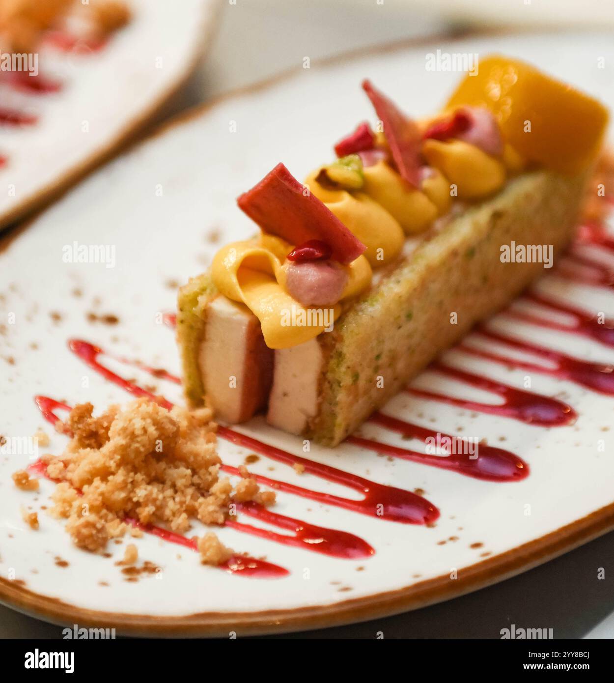 Obstkuchen mit Orangen-, Mango- und Erdbeersauce auf einem weißen Teller Stockfoto