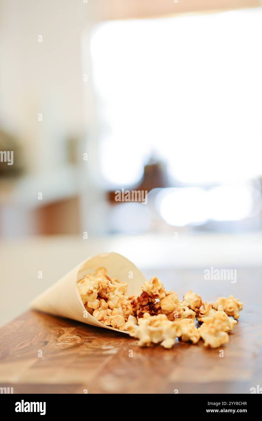 Karamell-Popcorn, das vom Papierkegel auf den Holztisch verschüttet wird. Stockfoto