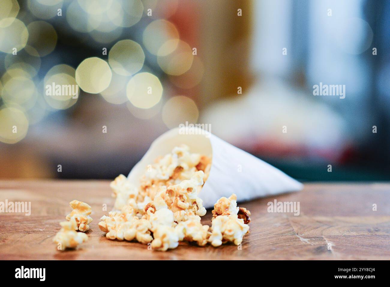 Karamell-Popcorn mit Bokeh-Lichtern, die von einem Papierkegel verschüttet werden. Stockfoto