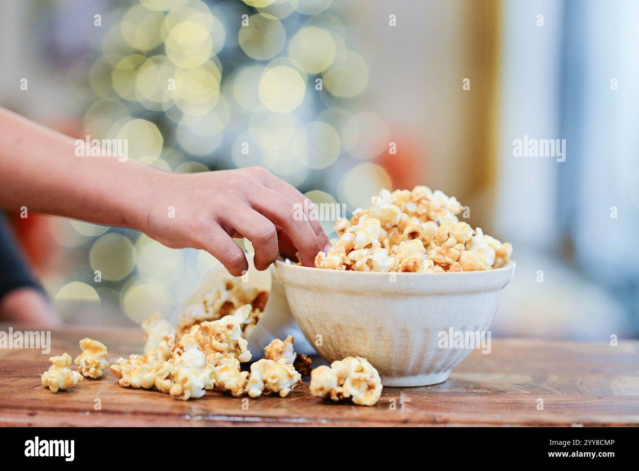 Die Hand greift nach Popcorn in einer Schüssel mit festlichen Bokeh-Lichtern. Stockfoto