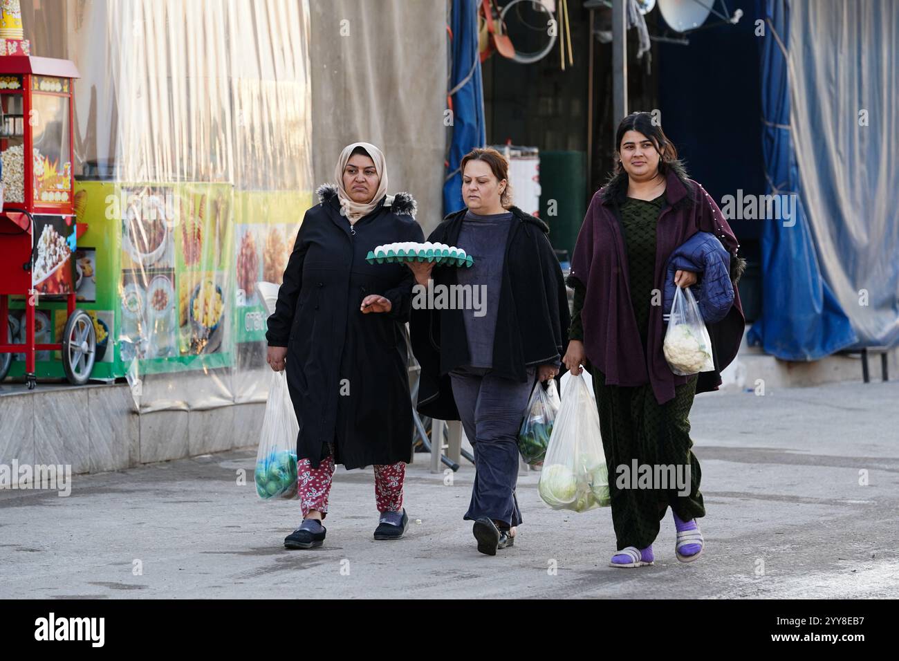 Frauen laufen auf der Straße im Lager Domiz für syrische kurdische Flüchtlinge etwa 18 km südwestlich von Duhok in der Region Kurdistan. Die Provinz Duhok beherbergt 92.000 syrische Flüchtlinge von 275.000 Flüchtlingen in der Region Kurdistan im Irak, die seit Ausbruch der syrischen Revolution im Jahr 2011 migriert sind. Die meisten von ihnen weigern sich, trotz des Sturzes des Baschar al-Assad-Regimes in ihr Land zurückzukehren, aus Angst vor dem Ausbruch bewaffneter Konflikte zwischen den syrischen Demokratischen Kräften (SDF) und der von der Türkei unterstützten syrischen Nationalarmee oder mit Hayat Tahrir al-Sham und anderen Oppositionskräften, die sich im Stich gesetzt haben Stockfoto