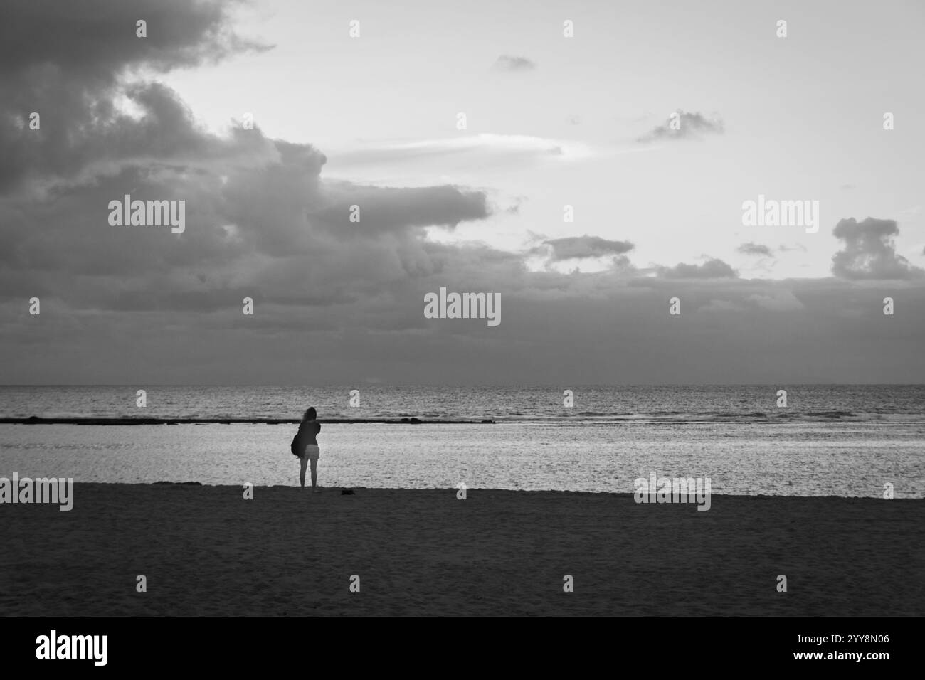 Eine einsame Figur, die bei Sonnenuntergang am Strand auf den Kanarischen Inseln in Spanien am Meer steht Stockfoto