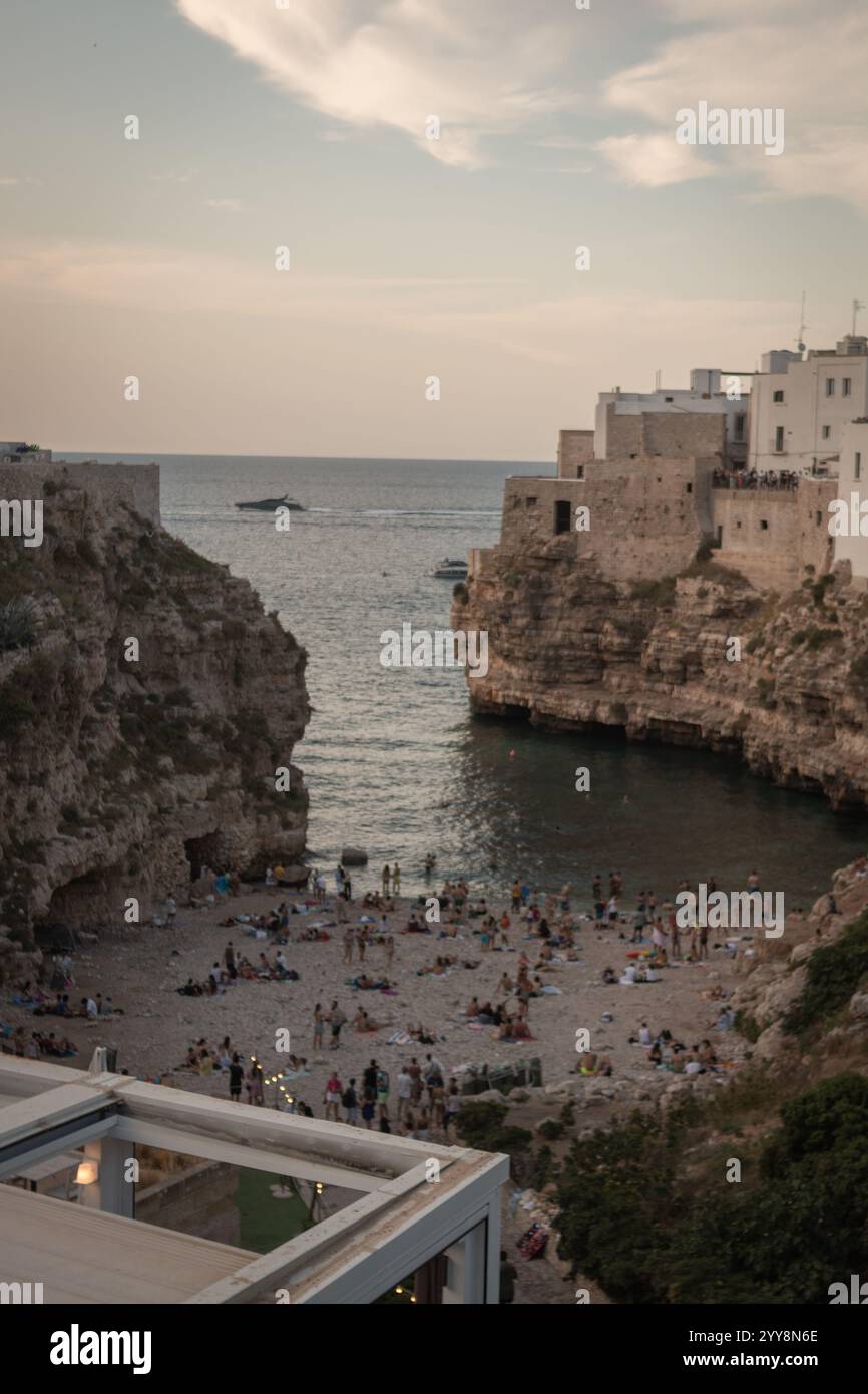 Ein atemberaubender Blick auf einen versteckten Strand, umgeben von dramatischen Klippen, mit Menschen, die einen Sommertag am Meer in Polignano a Mare, Italien, genießen. Stockfoto