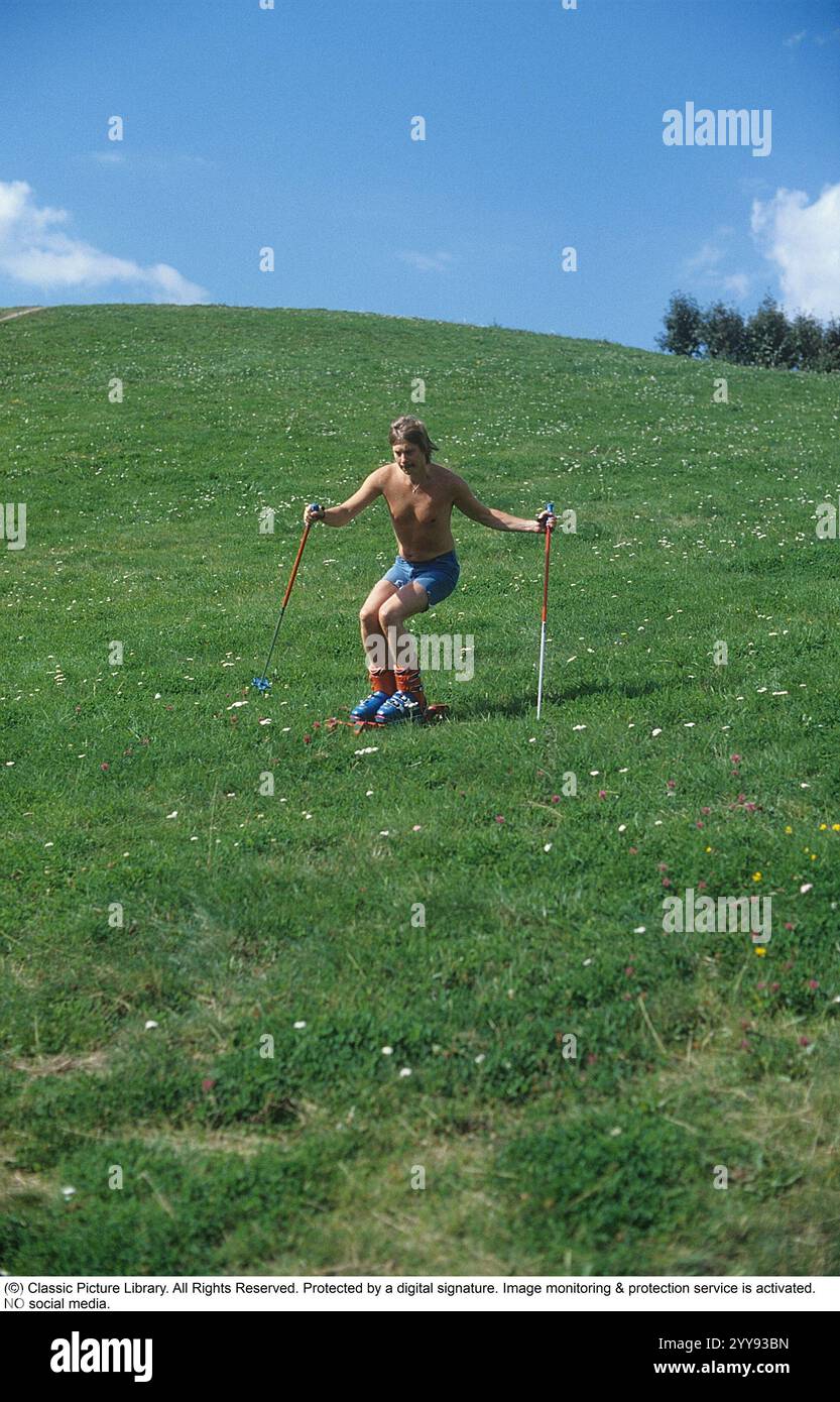 Slalom ohne Schnee. 1980 wird im Sommer eine neue Erfindung der Grasskier getestet. Die Skifahrer sind mit Rollbändern ausgestattet und hatten ähnliche Funktionen wie normale Skier. Ein Mann, der im Sommer auf einem grasbewachsenen Hügel die rollenden Skier probierte. In den 1980er Jahren gab es eine Handvoll Grasskihersteller Hier eine Webseite, die die Grasski-Geschichte erzählt: https://www.theskijournal.com/exclusive/grassholes/ Ref. DV25 Stockfoto