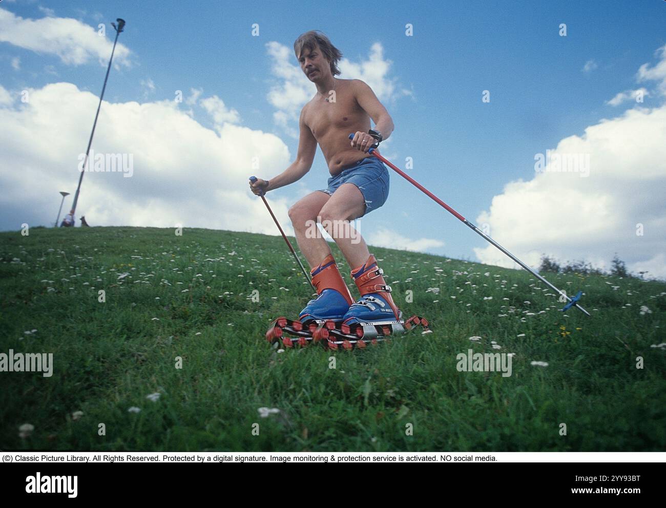 Slalom ohne Schnee. 1980 wird im Sommer eine neue Erfindung der Grasskier getestet. Die Skifahrer sind mit Rollbändern ausgestattet und hatten ähnliche Funktionen wie normale Skier. Ein Mann, der im Sommer auf einem grasbewachsenen Hügel die rollenden Skier probierte. In den 1980er Jahren gab es eine Handvoll Grasskihersteller Hier eine Webseite, die die Grasski-Geschichte erzählt: https://www.theskijournal.com/exclusive/grassholes/ Ref. DV25 Stockfoto