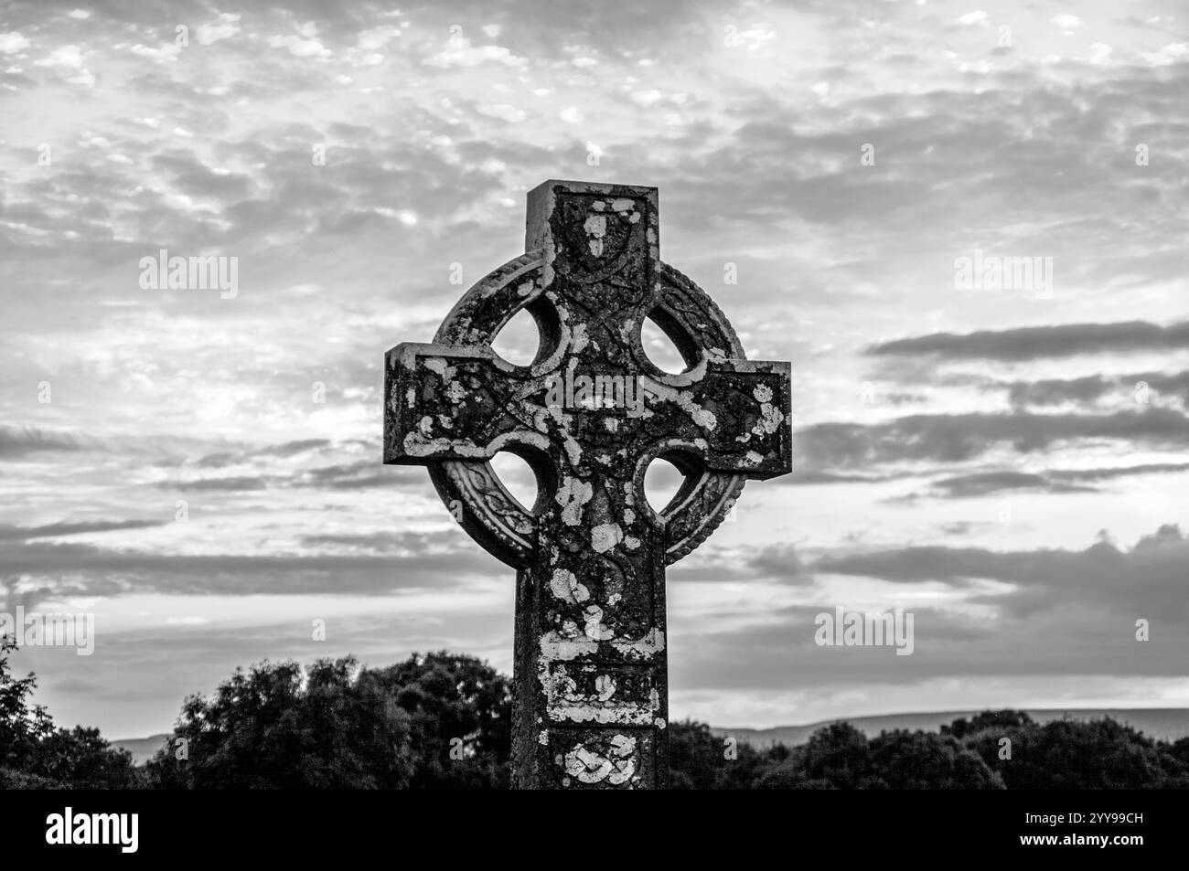 Ein Kreuz steht auf einem Feld mit bewölktem Himmel im Hintergrund. Das Kreuz ist alt und hat ein verwittertes Aussehen. Der Himmel ist bewölkt und gibt das S Stockfoto