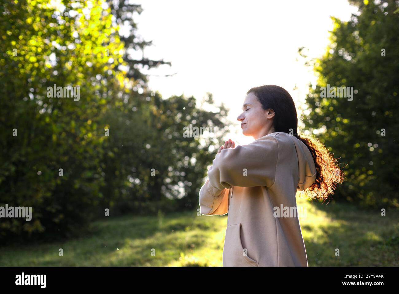 Frau mit lockigen Haaren, die Yoga-Namaste im Park praktiziert. Weibliche Silhouette bei Sonnenuntergang. Konzept von Vitalität, Gleichgewicht, Achtsamkeit, Ruhe, Entspannung. Stockfoto