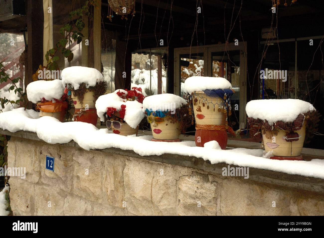 Göreme, Kappadokien, Turkiye - 26. November 2024: Auf der Hausterrasse werden mehrere dekorative Töpfe mit einzigartigen Gesichts-Motiven mit Schnee ausgestellt Stockfoto