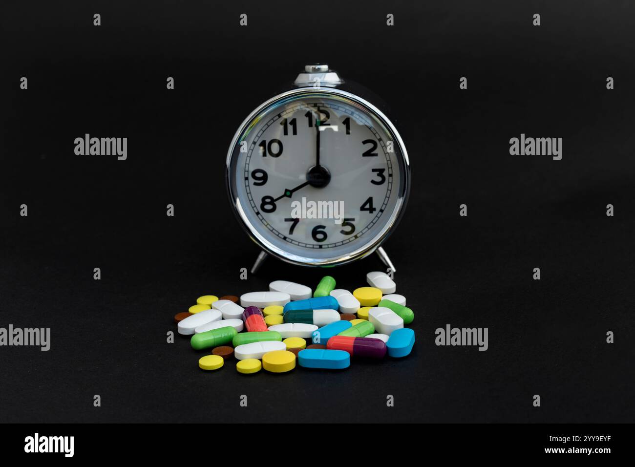 Wecker mit verschiedenen Pillen auf schwarzem Hintergrund Stockfoto