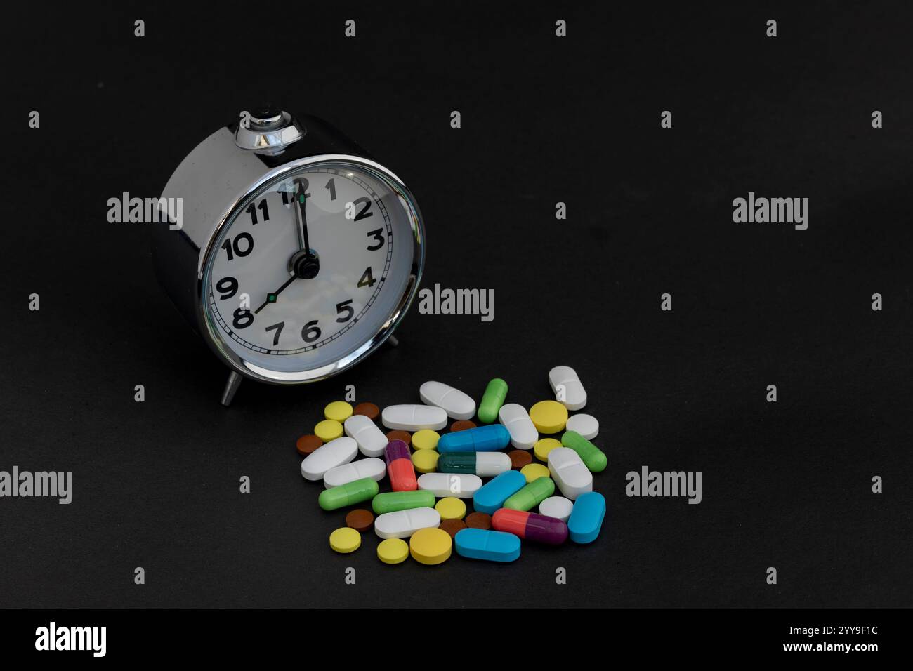 Wecker und mehrfarbige Pillen auf schwarzem Hintergrund Stockfoto