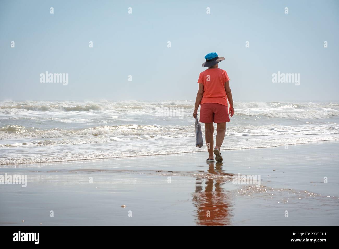 Frau, die in bunten Kleidern läuft und eine Plastiktüte neben dem Meer hält Stockfoto
