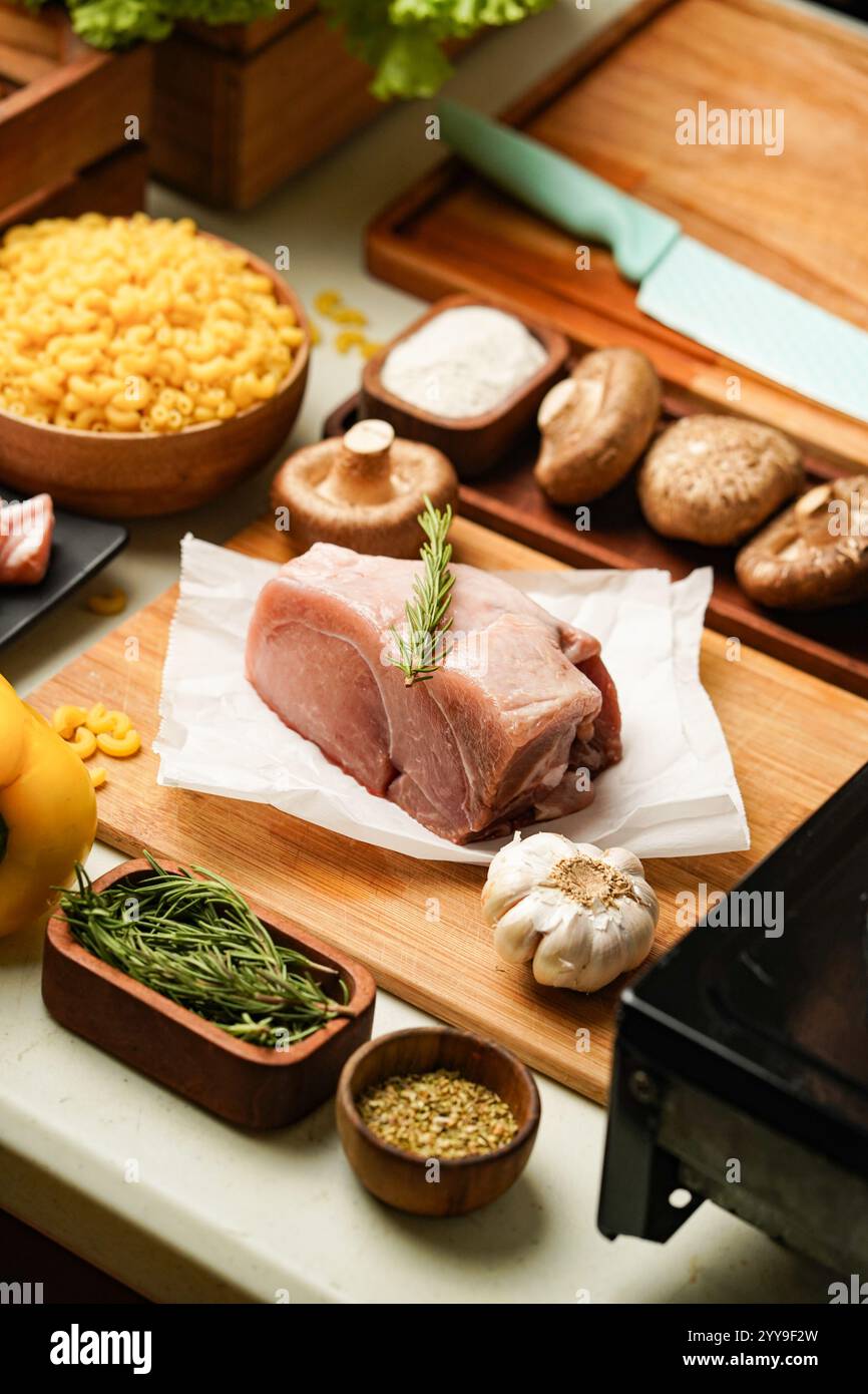 Frisch geschnittene Schweineschulter auf einem rustikalen Holzbrett, umgeben von lebendigem Gemüse und Gewürzen – bereit für eine herzhafte hausgemachte Mahlzeit. Stockfoto