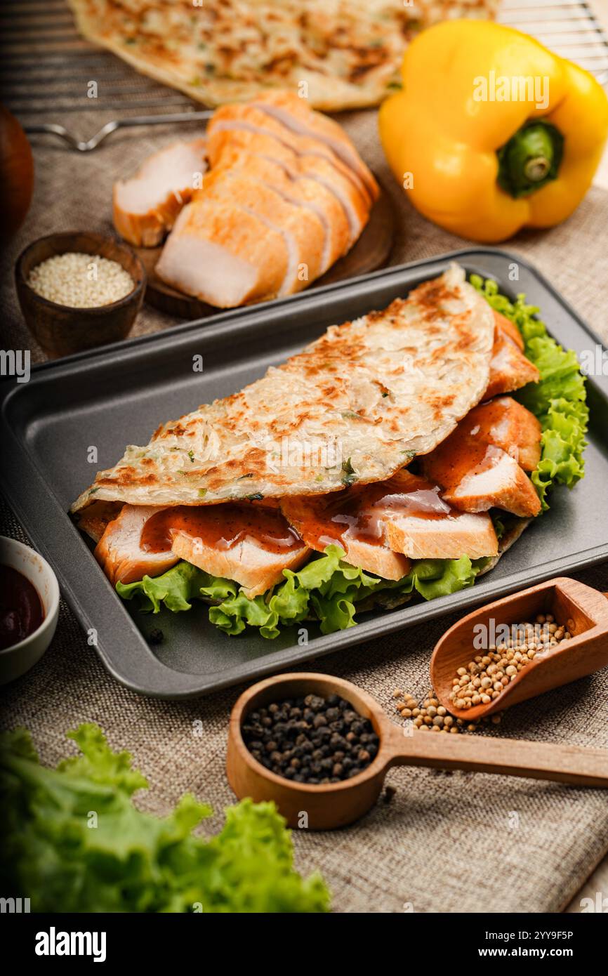 Herzhaftes Rindfleisch, gewickelt in ein blättriges, goldbraunes Fladenbrot mit knusprigem Salat, umgeben von frischen Zutaten wie Knoblauch, Schalotten und Chili Stockfoto