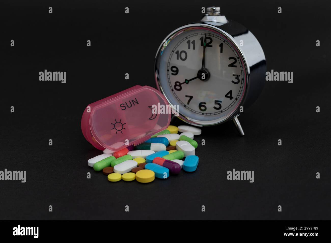 Wecker mit einer Pillen-Organizer-Box und Pillen auf schwarzem Hintergrund. Stockfoto