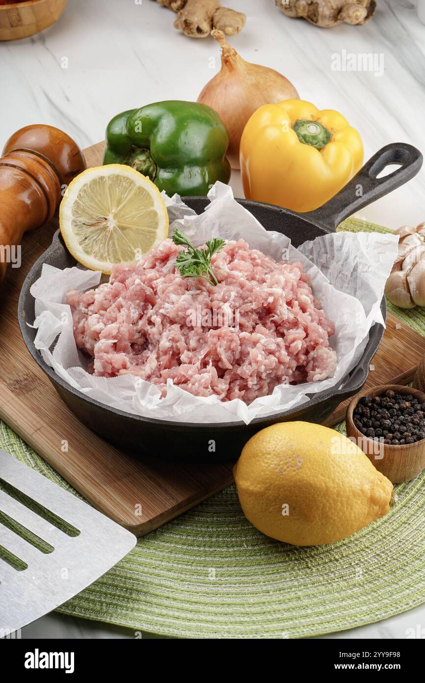 Eine rustikale Küchenszene mit frisch gemahlenem Schweinefleisch, umgeben von Bauerngemüse, aromatischen Gewürzen und natürlichen Zutaten, perfekt für hausgemachte Köche Stockfoto