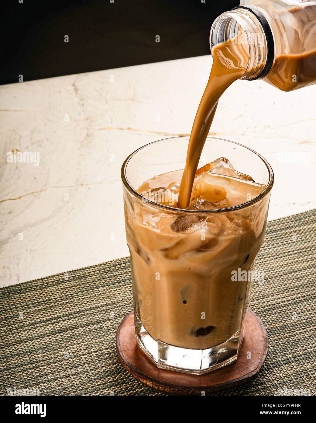 Ein erfrischender Eiskaffee, der in ein mit Eiswürfeln gefülltes Glas gegossen wird, fängt den satten Wirbel und die geschmeidige Textur eines gekühlten, cremigen Getränks ein Stockfoto