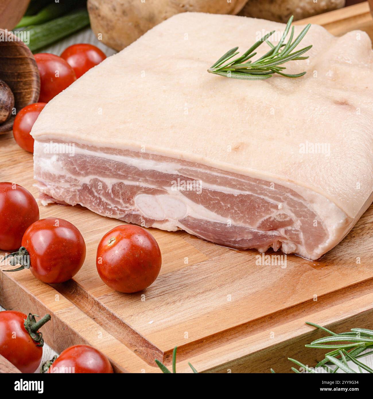 Frische, rohe Schweinebauchplatte mit Haut, garniert mit Rosmarin, Kirschtomaten, Chili, Meersalz, und schwarze Pfeffer auf rustikalem Papier – ideal Stockfoto
