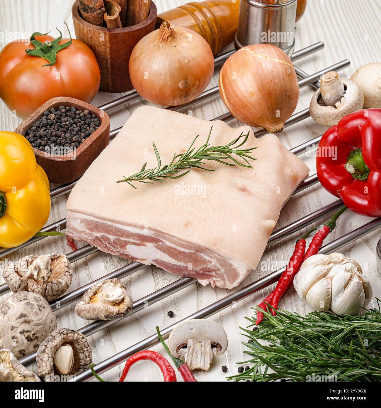 Frische, rohe Schweinebauchplatte mit Haut, garniert mit Rosmarin, Kirschtomaten, Chili, Meersalz, und schwarze Pfeffer auf rustikalem Papier – ideal Stockfoto